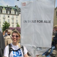 Smilende dame med banner som det står "En skole for Alle" på