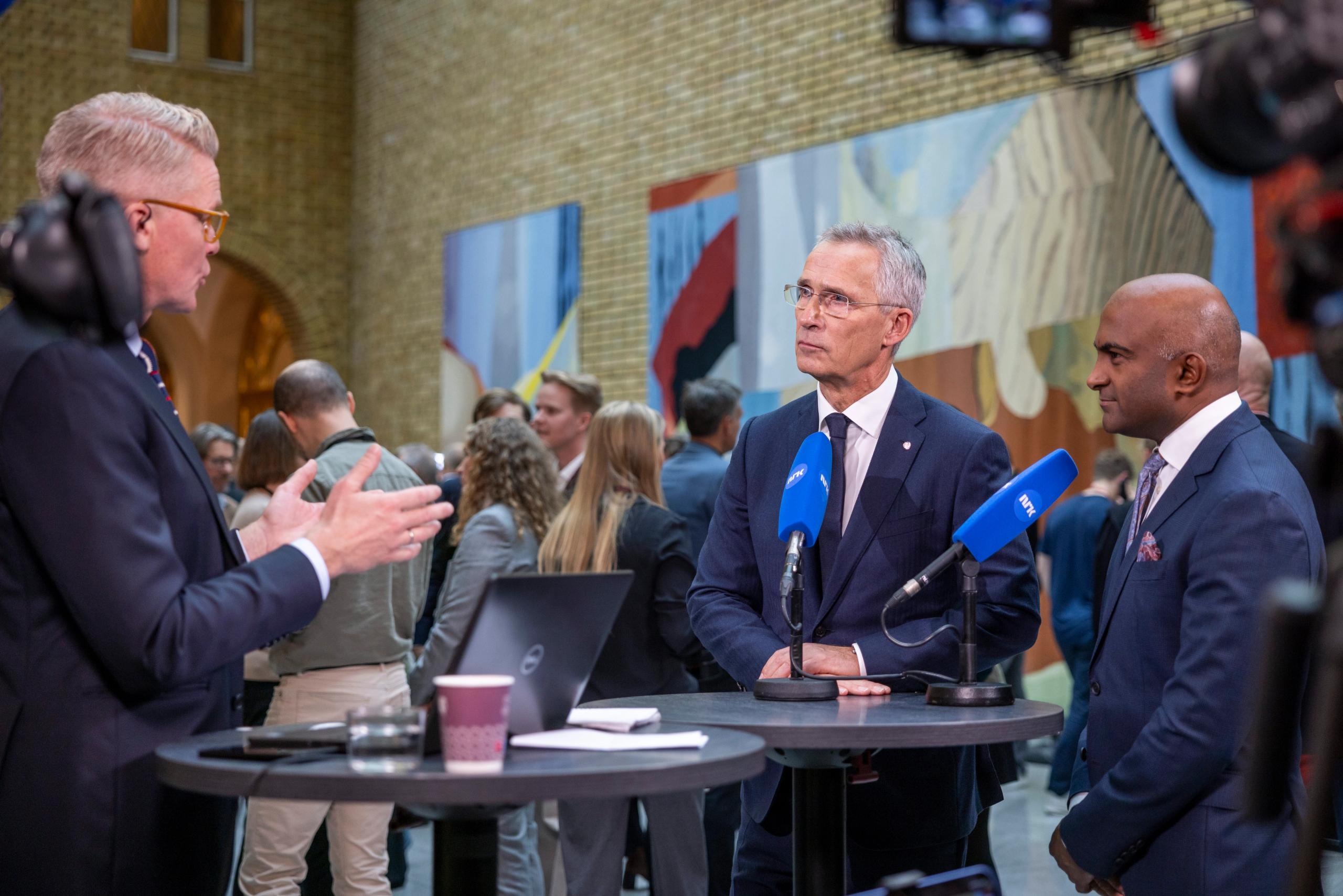 3 menn i dress, i vandrehallen på Stortinget, Jens Stoltenberg intervjues av NRK om statsbudsjettet.